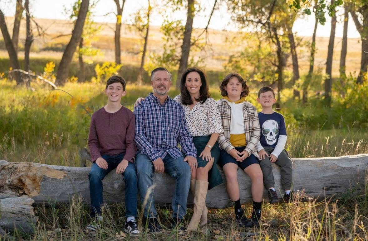 Julie with her husband and three sons, now young men, sitting on a log outdoors