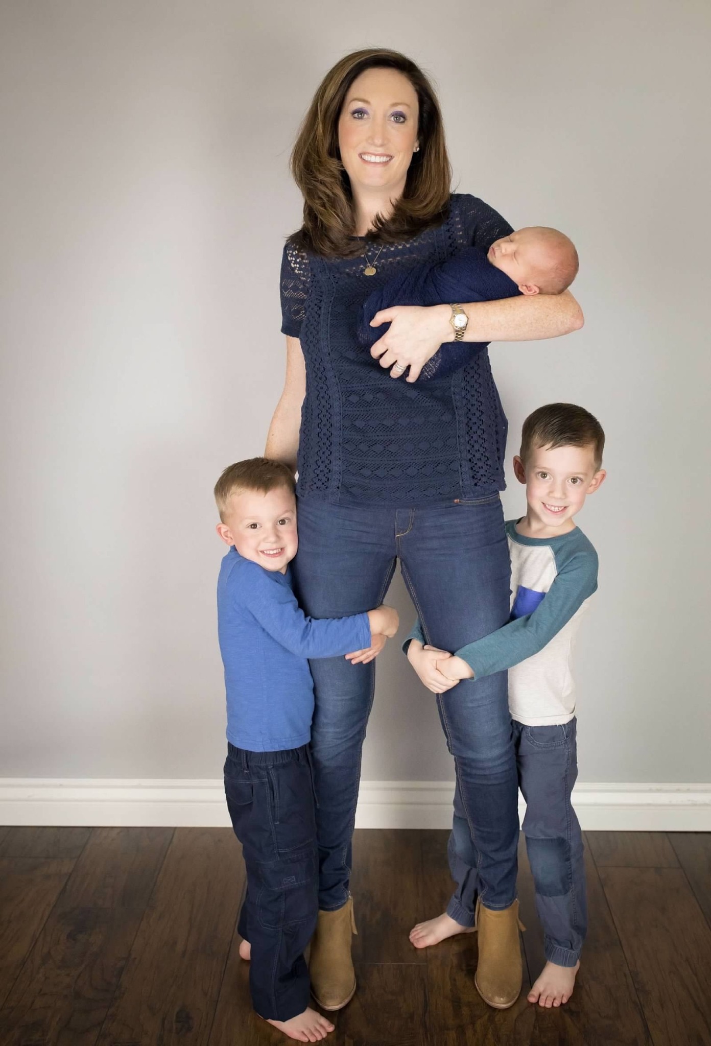 Julie holding her newborn while her two older boys hug her legs